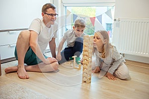 Young happy father playing with his two cute children with wooden blocks