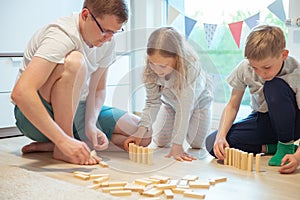 Young happy father playing with his two cute children with wooden blocks