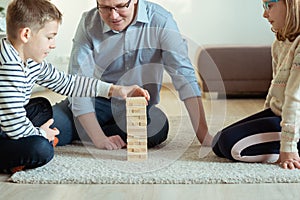 Young happy father playing with his two cute children with wooden blocks