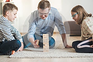 Young happy father playing with his two cute children with wooden blocks