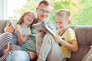 Young happy father reading book with cute children at home