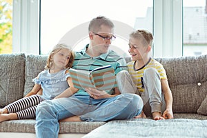 Young happy father reading book with cute children at home