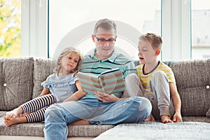 Young happy father reading book with cute children at home