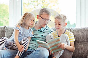 Young happy father reading book with cute children at home