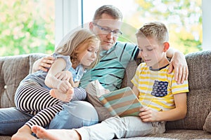 Young happy father reading book with cute children at home