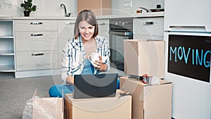 Young happy female with a cup of tea using her laptop on boxes for moving out and packing