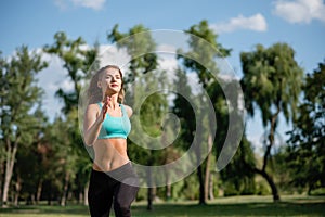 Young happy female runner running in city park. Healthy fitness woman jogging outdoors