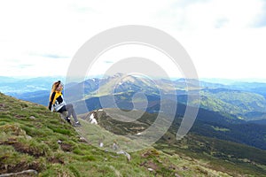 Young happy female tourist wearing yellow jacket sitting in Appenine mountains.