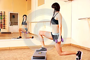 Young happy fit woman doing exercises with dumbells on step board