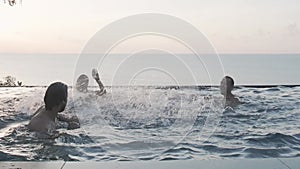 Young happy friends having fun in the view pool at sunset. Splashing water in the pool. Happy people on vacation. Traveling with