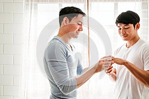 Young happy gay couple in love, proposing and marriage surprise wear a wedding ring in the living room at home. Gay men proposal