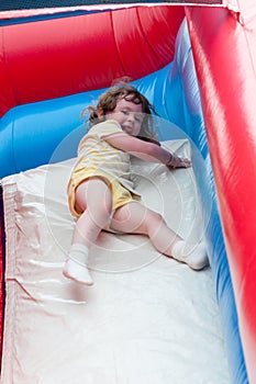 Young happy girl child riding inflatable slide outdoors on a warm summer day.