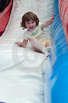 Young happy girl child riding inflatable slide outdoors on a warm summer day.