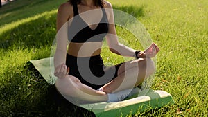Young happy girl doing yoga in the park, listening to music with headphones, sitting in lotus position