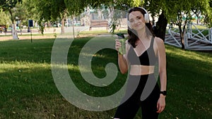 Young happy girl doing yoga in the park, listening to music with headphones, sitting in lotus position