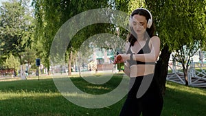 Young happy girl doing yoga in the park, listening to music with headphones, sitting in lotus position