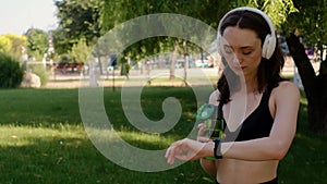 Young happy girl doing yoga in the park, listening to music with headphones, sitting in lotus position