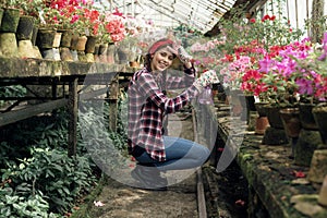 Young happy girl gardener in a plaid shirt with a red headband watering flowers