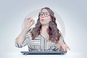 Young happy girl with glasses at the computer holds in her hand bitcoin. Digital money concept