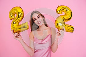 Young happy girl holds gold foil balloon isolated on pink background. BIRTHDAY PARTY concept