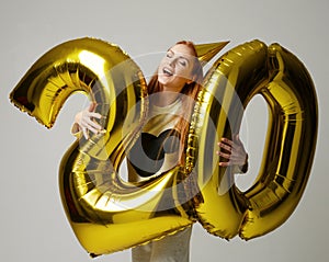 Young happy girl with huge gold digit twenty balloons as a present for birthday