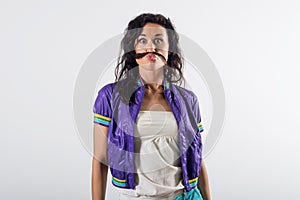 Young happy girl laughing, holding her hair, imitating mustache , wearing trendy outfit.