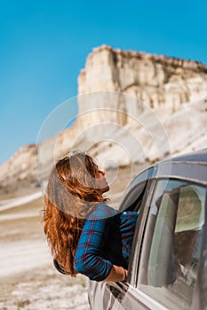 A young happy girl leans out of a car window on a trip to Crimea against a White rock background, concept of freedom