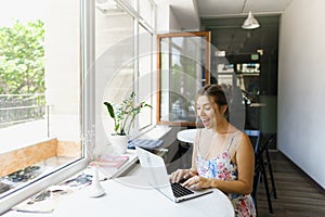 Young happy girl sitting at cafe and surfing internet by laptop.