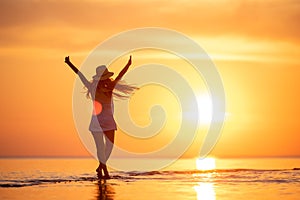 Young happy girl at sunset beach with raised arms