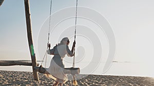 Young happy girl sway on swings, enjoy serene sea paradise relax, dream sunshine