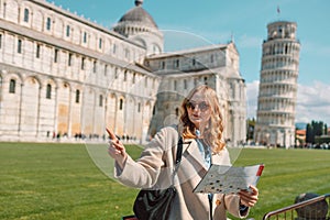 Young happy girl with toristic map on travel to Pisa. Tourist traveling visiting The Leaning Tower of Pisa.