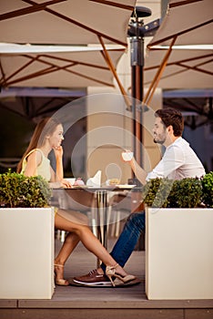 Young happy gorgeous lady is sitting in light cafe`s terrace outdoors on a sunny day and flirt with her leg with partner, while sm