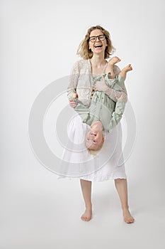 Young happy gorgeous woman mother holding amazing little girl daughter upside down having fun, playing games. Childhood.