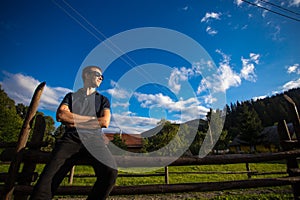 A young happy handsome man in sunglasses resting on a wooden handmade fence in garden