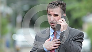 Young happy Hispanic businessman talking on the phone outdoors