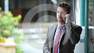 Young happy Hispanic businessman talking on the phone outdoors