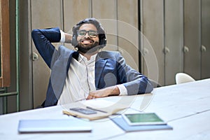 Young happy indian business man wearing headphones sitting at workplace.