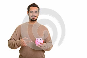 Young happy Indian man holding piggy bank and pointing finger