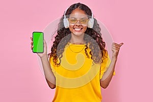 Young happy Indian woman teenager in wireless headphones holding mobile phone