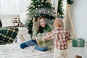 Young happy kind redhead diverse woman holds out a gift box to a child.