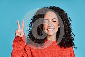 Young happy latin woman having fun showing peace hand sign isolated on blue.