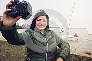 young happy latin woman taking a selfie with her camera with the river and boats on background