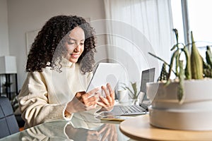 Young happy latin woman using digital tablet at home looking at tab.