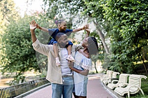 Young happy laughing African couple parents, spending time together and enjoying warm summer evening in park, walking