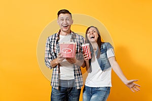 Young happy laughing couple woman man in casual clothes watching movie film on date holding bucket of popcorn plastic