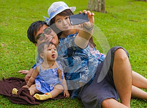 Young happy loving Asian Japanese family with parents and sweet baby daughter at city park together with father taking selfie pic