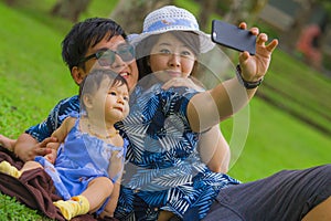 Young happy loving Asian Japanese family with parents and sweet baby daughter at city park together with father taking selfie pic