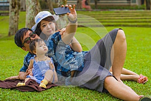 Young happy loving Asian Korean family with parents and sweet baby daughter at city park together with father taking selfie pic