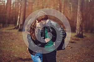 Young happy loving couple in leather jackets hugs outdoor on cozy walk in forest