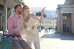 Young happy loving couple looking at map and sitting on scooter